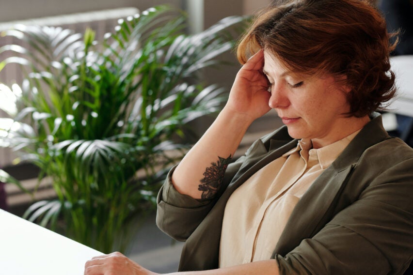 Photo of woman working on laptop, holding head, looking frustrated