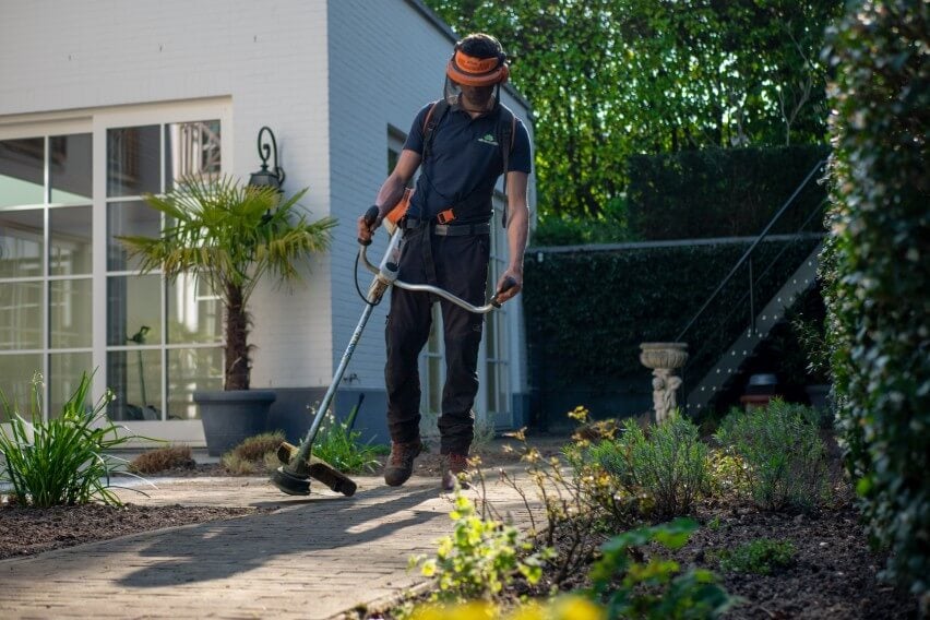 landscaping worker operating a lawn trimmer in front of house