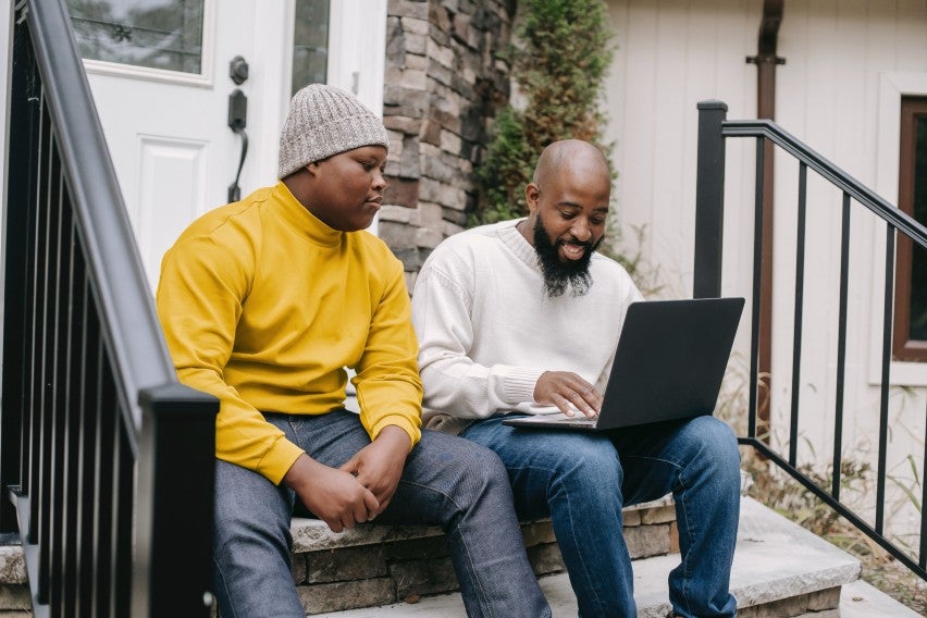 two men sitting on stoop with laptop smiling