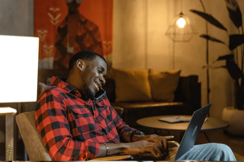 Man sitting in living room smiling at laptop while on the phone