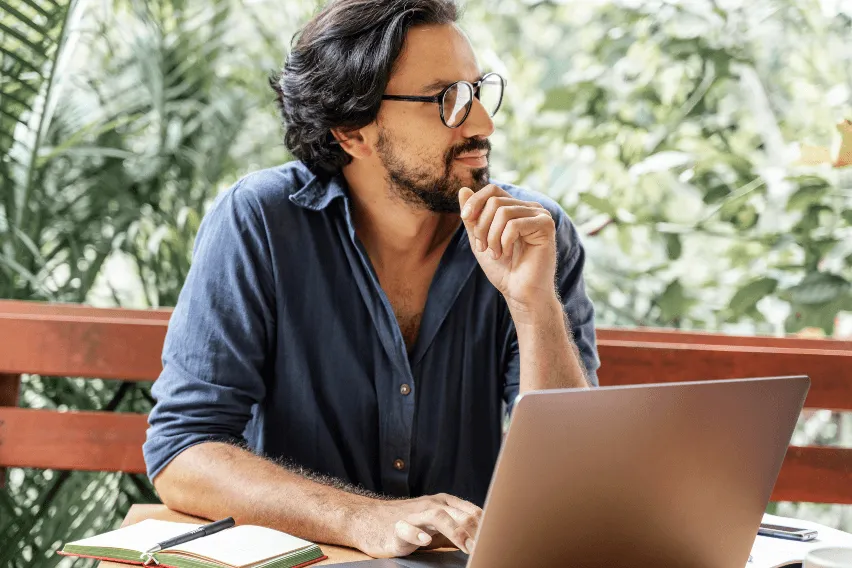 Man sits at laptop looking away from camera lost in thought