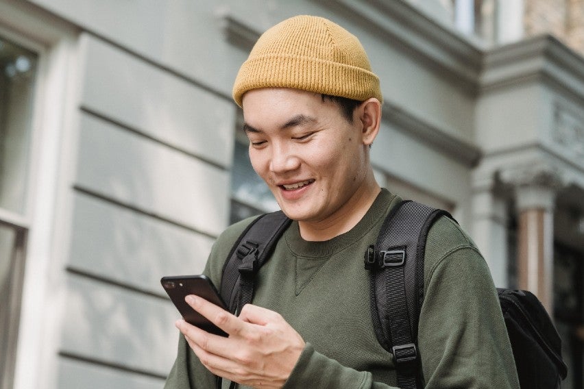 man with hat walking down street looking at phone and smiling